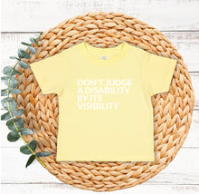 Load image into Gallery viewer, Toddler t-shirt with the phrase “Don’t judge a disability by its visibility” in white vinyl, designed for disability awareness and inclusion. Available in multiple colors, including maroon and blue.