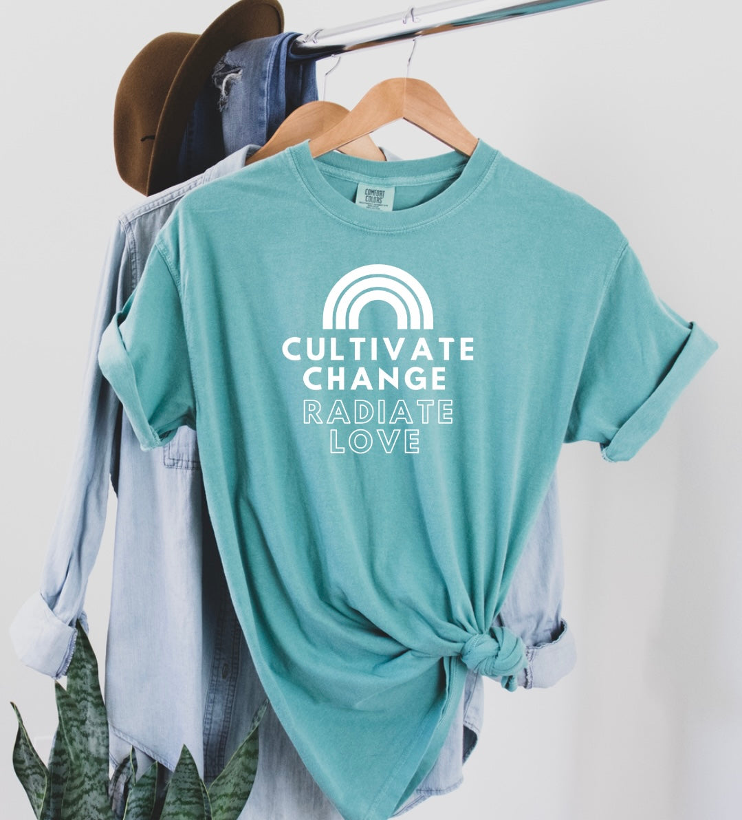 Say hello threads comfort colors shirts in the color seafoam with white font that reads cultivate change radiate love and has a white rainbow at the top of the print.