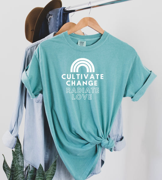 Say hello threads comfort colors shirts in the color seafoam with white font that reads cultivate change radiate love and has a white rainbow at the top of the print.