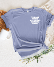 Load image into Gallery viewer, say hello threads shirt with the words you are wildly capable of amazing things on the pocket and on the back of the shirt in large font. 
