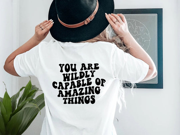 say hello threads white shirt with the words you are wildly capable of amazing things in large black font on the back of the shirt. 