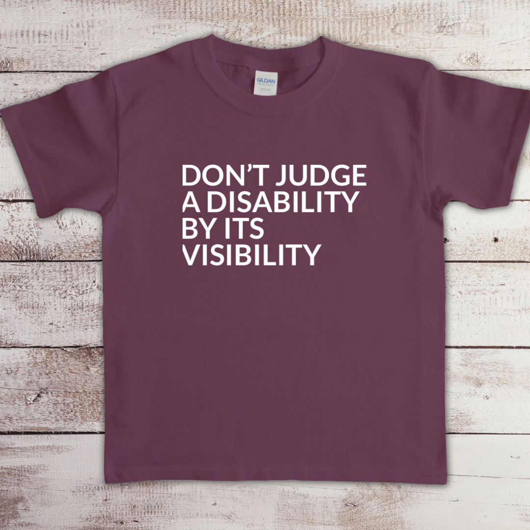 Toddler t-shirt with the phrase “Don’t judge a disability by its visibility” in white vinyl, designed for disability awareness and inclusion. Available in multiple colors, including maroon and blue.