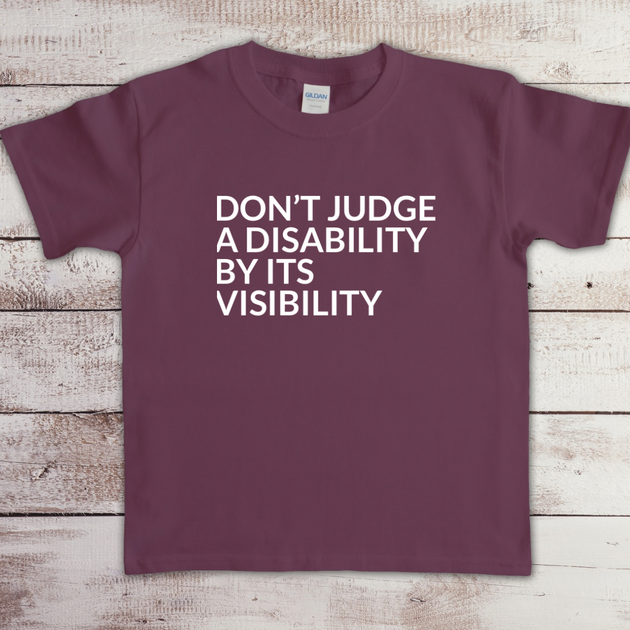 Toddler t-shirt with the phrase “Don’t judge a disability by its visibility” in white vinyl, designed for disability awareness and inclusion. Available in multiple colors, including maroon and blue.