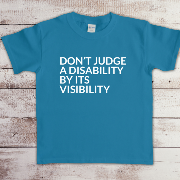 Toddler t-shirt with the phrase “Don’t judge a disability by its visibility” in white vinyl, designed for disability awareness and inclusion. Available in multiple colors, including maroon and blue.